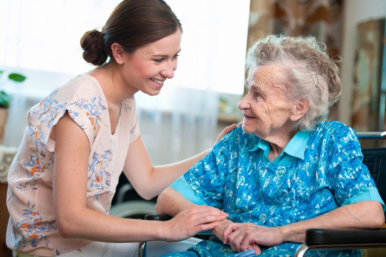 A woman is holding the hand of an older lady.