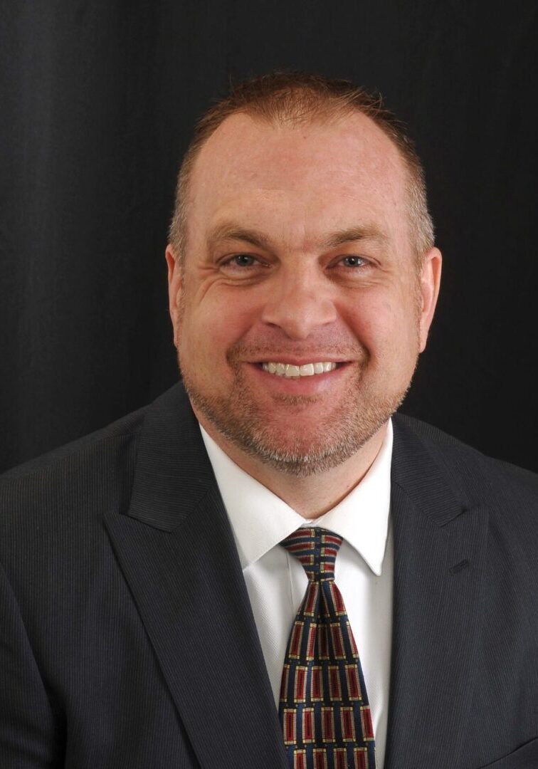 A man in a suit and tie smiling for the camera.